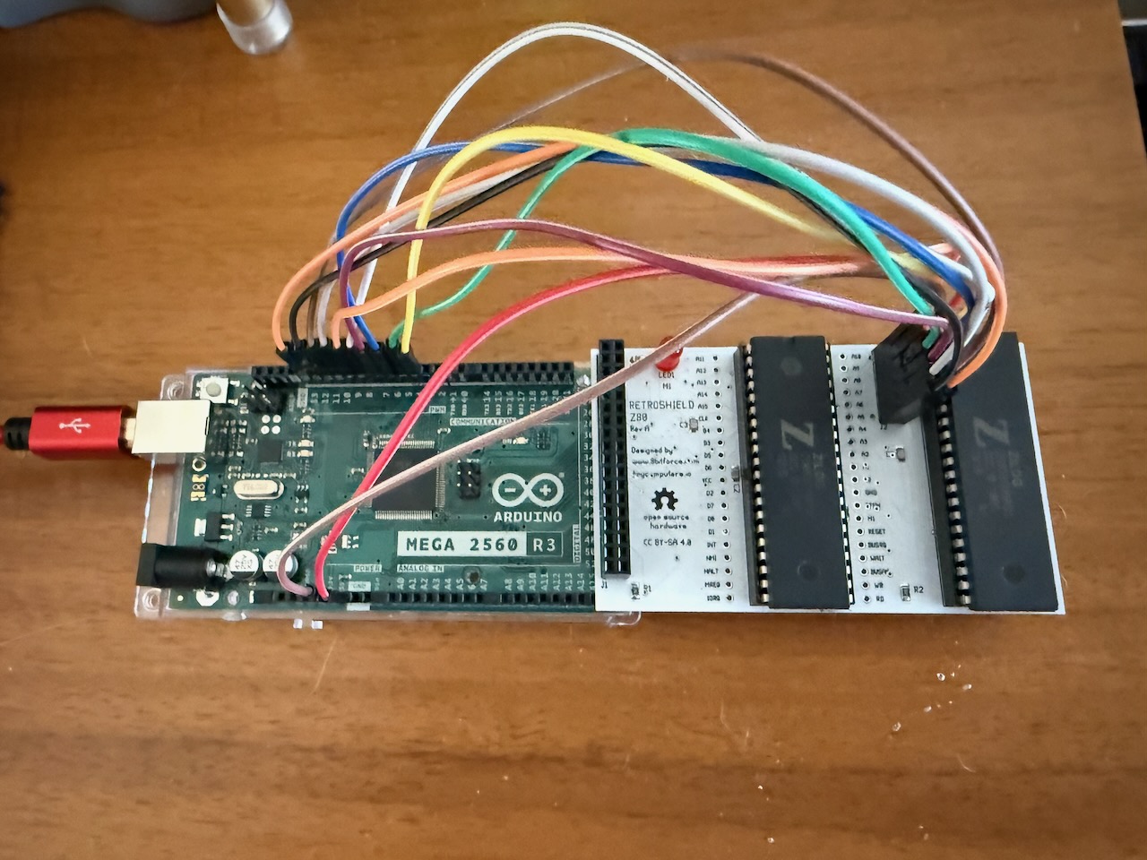 The assembled dual Z80 RetroShield plugged into an Arduino Mega 2560, with colored jumper wires running from the J2 control header to the Mega's free digital pins