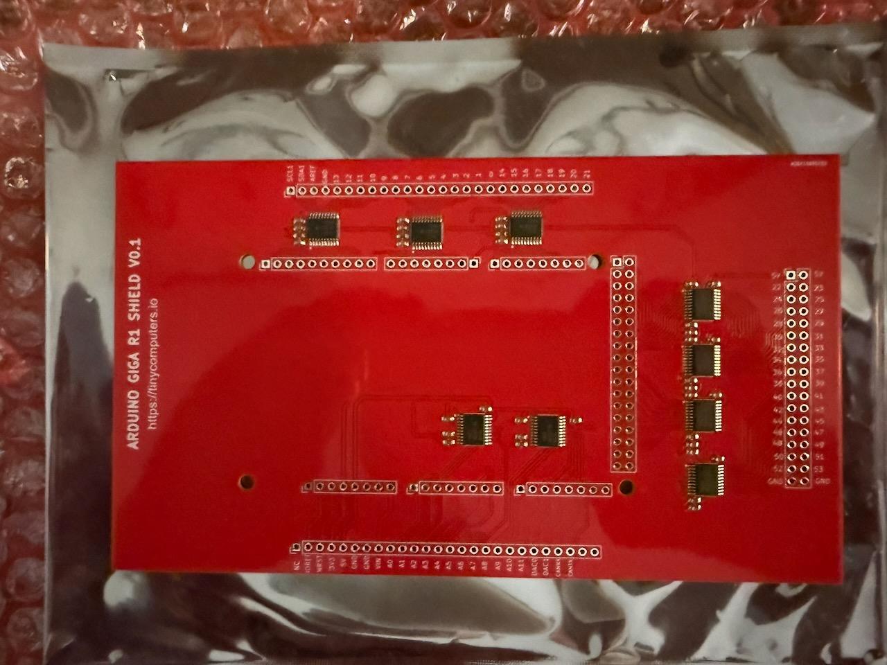 The bare Arduino Giga R1 Shield V0.1 PCB — a red board with nine TXB0108 level converter ICs in antistatic packaging