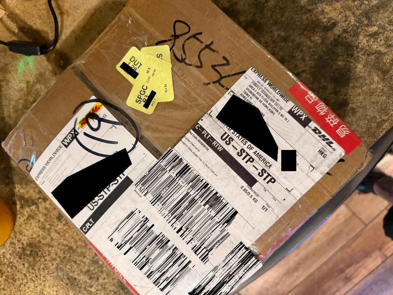 The shipping box as it arrived, wrapped in plastic with two DHL Express Worldwide waybills, origin Hong Kong, recipient details blacked out